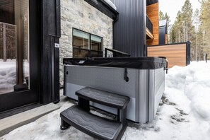 Un edificio moderno con fachada de piedra, un jacuzzi grande y una terraza de madera.