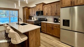 Une cuisine moderne avec des meubles en bois, des appareils en acier inoxydable, un grand îlot central doté de tabourets de bar et une vue sur un paysage enneigé par une grande fenêtre.