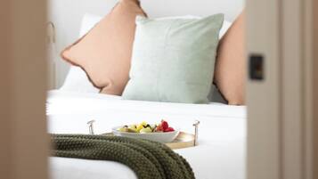 Une chambre à coucher avec un lit, des oreillers, une couverture verte en tricot, un panier de fruits et une étagère murale décorative.