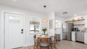 A modern kitchen with a dining area, featuring a round wooden table, chairs, and a hanging light fixture. - Walk to UF/Stadium | Near Shands/Downtown (NEW!) (Gainesville)