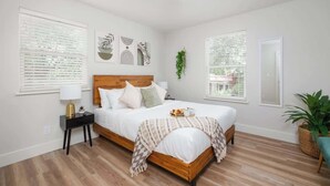 A bedroom with a wooden bed, white bedding, a bedside table with a lamp, and artwork on the wall. - Walk to UF/Stadium | Near Shands/Downtown (NEW!) (Gainesville)