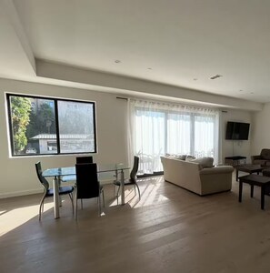 Amplia sala de estar con un ventanal grande, un sofá, una zona de comedor con sillas y un televisor de pantalla plana montado en la pared.
