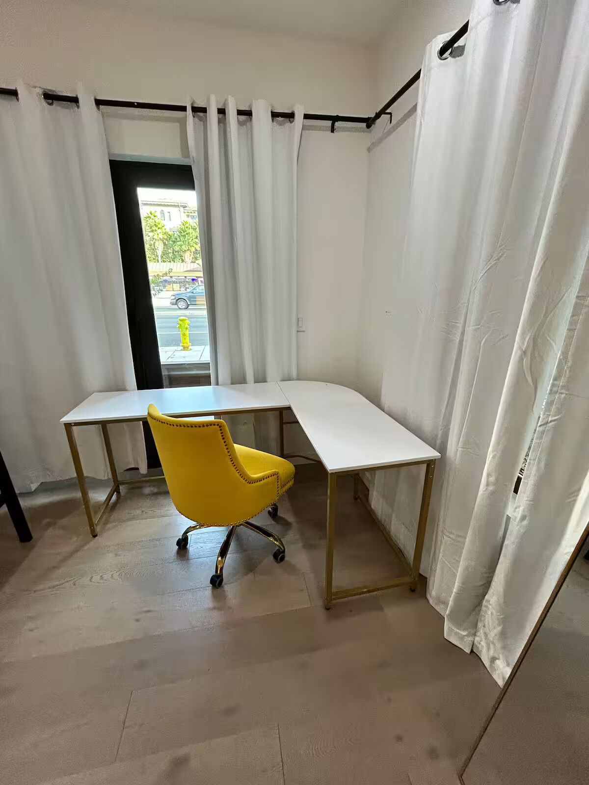 A room with a white desk, a yellow office chair, and white curtains.