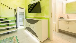 Ein modernes Badezimmer mit einer grünen Akzentwand, einem flachbildfernseher über dem Waschbecken und einer Treppe zu einem anderen Raum.
