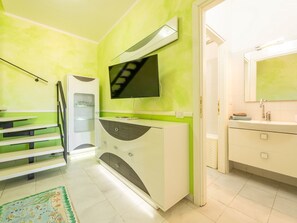 A modern bathroom with a green wall, a TV mounted above the sink, and a staircase leading to another room. - Apartment Parigi by Interhome (Villasimius)