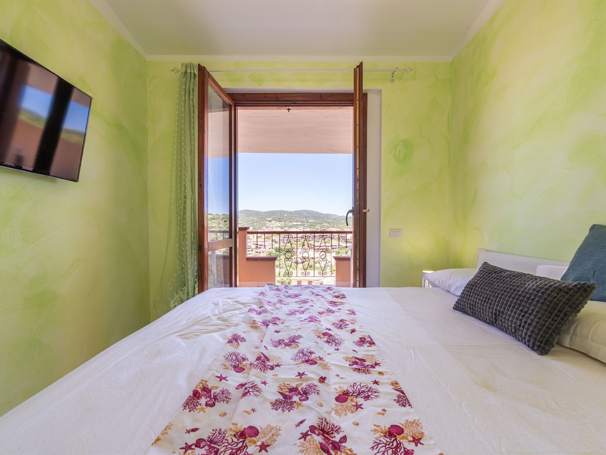 Un dormitorio con cama, televisor y balcón con vistas.