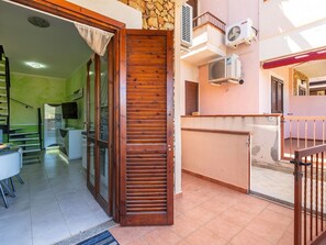 A residential interior with a wooden door, tiled floor, and a kitchen area with a refrigerator and stove. - Apartment Parigi by Interhome (Villasimius)