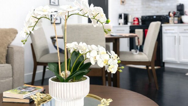 Une table ronde en bois sur laquelle se trouve un vase blanc contenant des orchidées blanches, un livre et un objet décoratif doré.