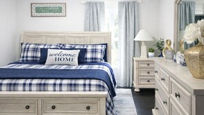 Une chambre à coucher avec un lit, une commode, un miroir et une fenêtre avec des rideaux.