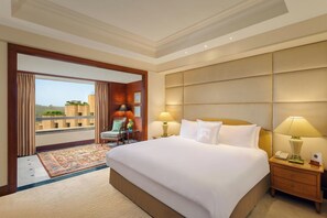 A hotel room with a large bed, two bedside tables with lamps, a chair, a small table with a vase, and a view of a building through a glass door. - ITC Maurya, a Luxury Collection Hotel (New Delhi)