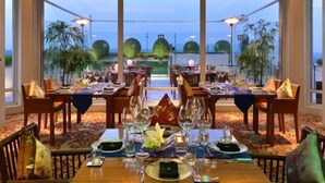 A restaurant with tables set for dining, large windows offering a view of the sea and greenery, and a warm interior lighting. - ITC Maurya, a Luxury Collection Hotel (New Delhi)