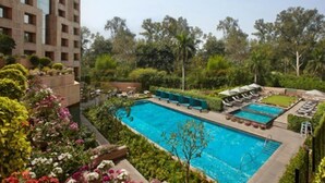 A swimming pool surrounded by lush greenery and a multi-story building. - ITC Maurya, a Luxury Collection Hotel (New Delhi)