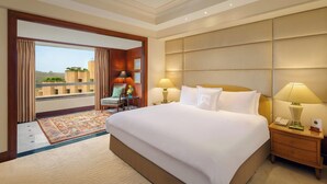 A hotel room with a large bed, two bedside lamps, a nightstand, a chair, and a view of the city through a large window. - ITC Maurya, a Luxury Collection Hotel (New Delhi)