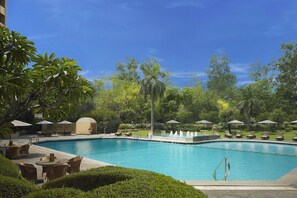 A swimming pool with lounge chairs and umbrellas, surrounded by greenery and a clear sky. - ITC Maurya, a Luxury Collection Hotel (New Delhi)