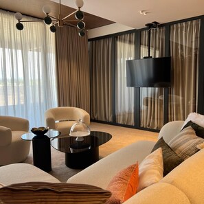 A modern living room with a sofa, armchairs, a coffee table, and a TV mounted on the wall. - Aria Hotel (Mahala)