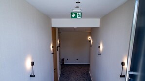 A carpeted staircase with a ceiling sign, wall-mounted lights, and a door on the right. - Aria Hotel (Mahala)