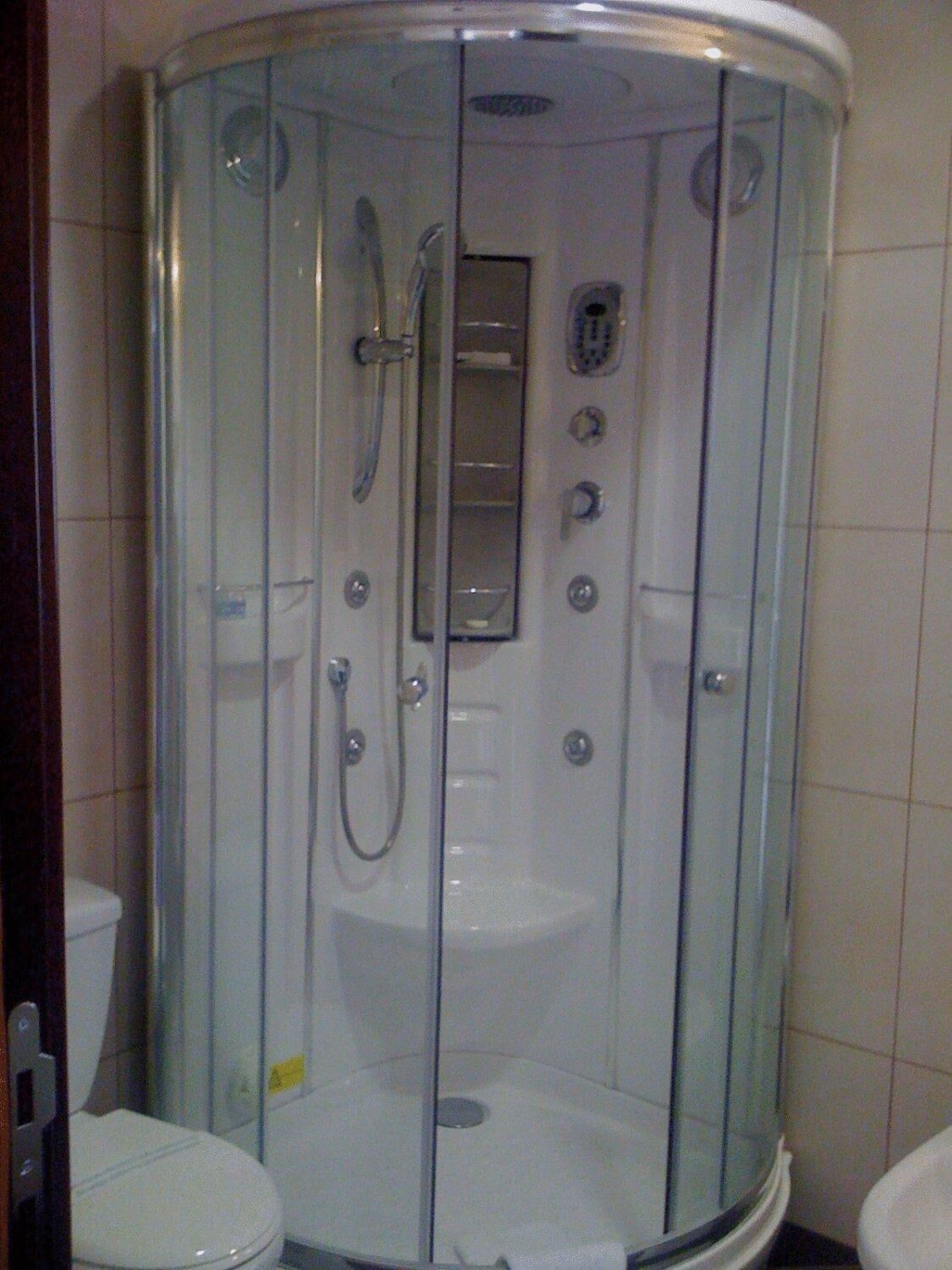 A glass-enclosed shower stall with a handheld showerhead and a wall-mounted control panel.