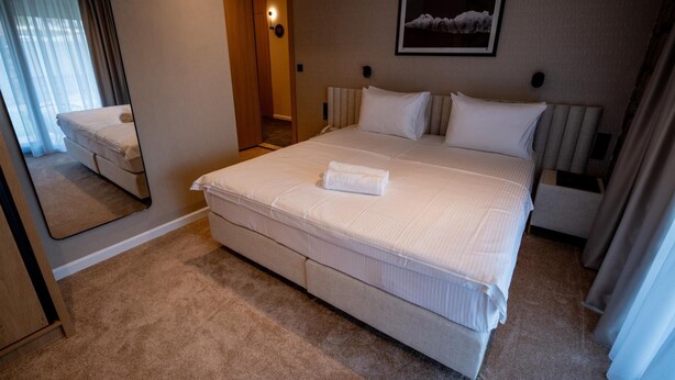A hotel room with a large bed, a mirror, a framed picture on the wall, and a door leading to another room. - Aria Hotel (Mahala)