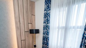 A modern room with a wooden accent wall, a plush orange armchair, a small round table, and a large window with sheer curtains. - Aria Hotel (Mahala)