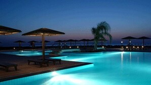 A nighttime pool area with illuminated edges, umbrellas, and lounge chairs.