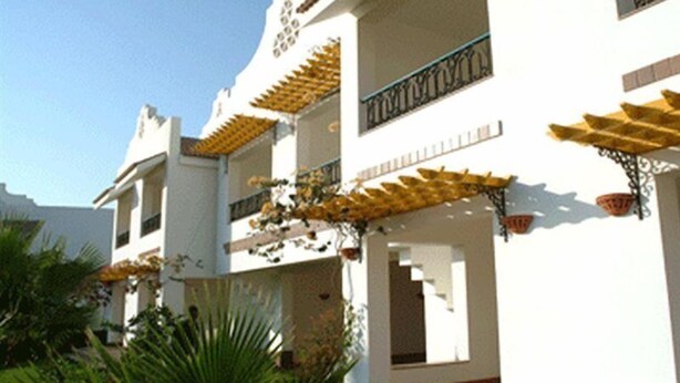 A multi-story building with balconies, a tiled roof, and a garden area with plants.