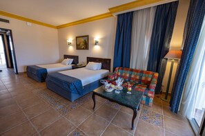 A hotel room with two beds, a small table with breakfast items, a colorful sofa, and a lamp.