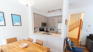 Ett modernt kök med rostfria vitvaror, en matplats med ett träbord och stolar samt en trappa som leder till ett annat våningsplan.