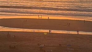 Ein Strand mit Menschen und Sonnenschirmen bei Sonnenuntergang.