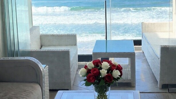 Ein modernes Wohnzimmer mit Meerblick, ausgestattet mit einem Glastisch mit Blumenvase, weißen Sofas und einem gemusterten Teppich.