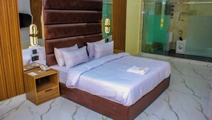 A modern hotel room with a large bed, wooden headboard, bedside tables, and a glass shower enclosure. - Soulmate Hotels & Suites Ojodu (Lagos)