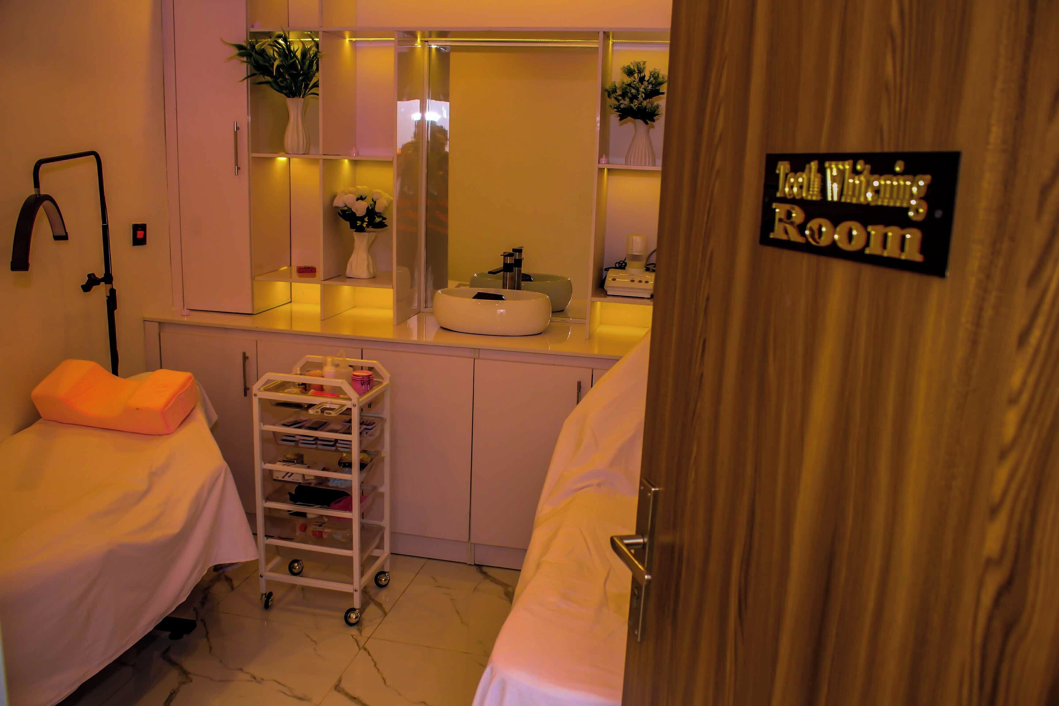A hotel room with a bed, a bedside table, a mirror, a sink, and a cart with toiletries.