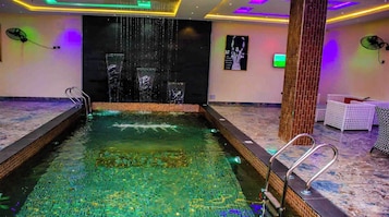 Piscina com cachoeira, cercada por espreguiçadeiras e um pilar de tijolos.