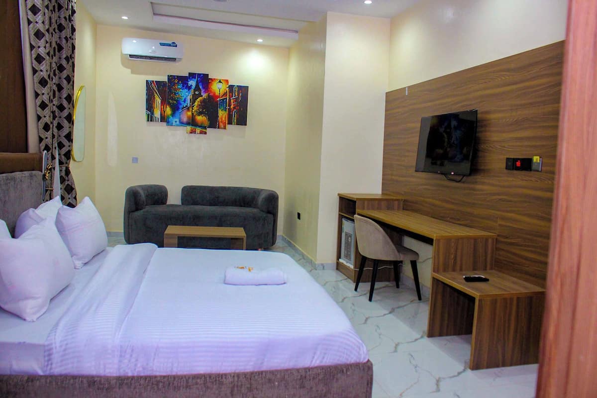 A hotel room with a bed, a desk, a chair, a TV, and a painting on the wall.