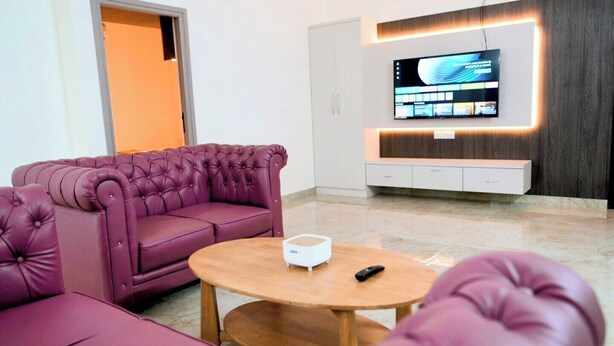 Un soggiorno moderno con un divano viola, un tavolino in legno e una TV a schermo piatto montata a parete.