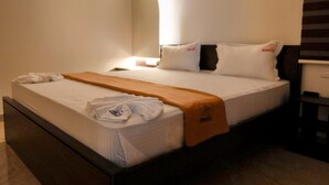 Un letto rifatto con un comofort bianco, un asciugamano bianco piegato e una coperta marrone.