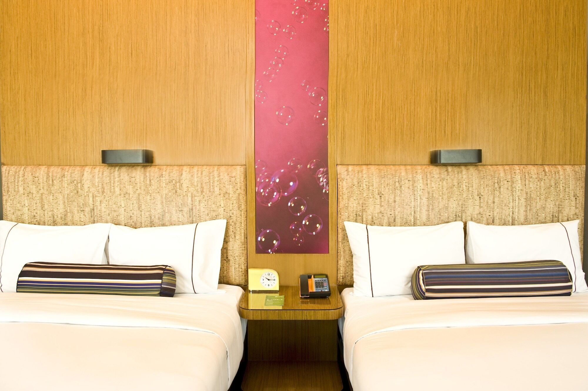 Une chambre d’hôtel avec deux lits, une table de chevet avec une horloge et un téléphone, et un mur orné d’un motif à bulles.