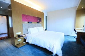 Une chambre d’hôtel moderne avec un grand lit, une tête de lit en bois, une table de chevet et un bureau avec une chaise.