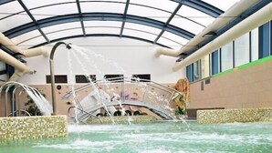 An indoor swimming pool with a glass ceiling, a water fountain, and a tiled edge. - Eger Park (Eger)