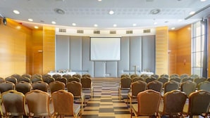 A conference room with rows of chairs facing a large screen, a podium, and a table with a laptop. - Eger Park (Eger)
