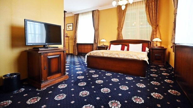A hotel room with a large bed, a television, two bedside tables, and a chandelier. - Eger Park (Eger)