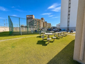 Un campo deportivo con un arco de fútbol, mesas de picnic y edificios al fondo.