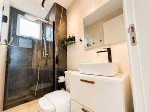 Un baño moderno con ducha acristalada, lavabo blanco y un espejo grande.
