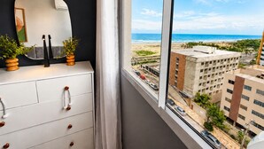 Een kamer met een dressoir, een spiegel en uitzicht op een strand en gebouwen.