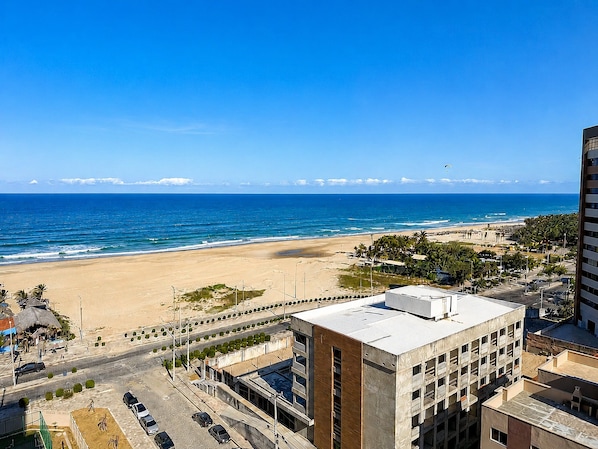 Un paisaje urbano costero con playa, una carretera con coches y un edificio de techo plano.