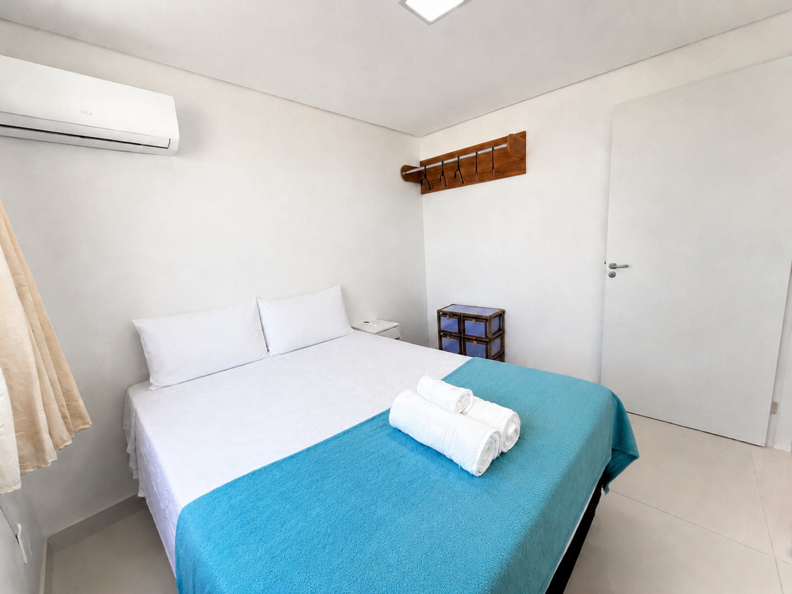 Habitación de hotel con una cama, un perchero de madera, una mesita y una puerta.