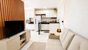 Een moderne woonkamer met een flatscreen televisie, een bank en een keuken in de achtergrond.