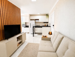 A modern living room with a flat-screen TV, a sofa, and a kitchen area in the background. - Hosts BR - Viva Praia do Futuro (Fortaleza)
