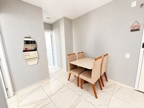 A dining area with a table and chairs, a kitchen in the background, and a hallway leading to another room.