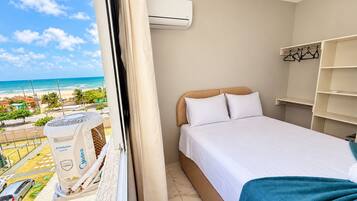 Ein Hotelzimmer mit Bett, Fenster und Klimaanlage, mit Blick auf den Strand.