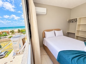 Habitación de hotel con cama, ventana con aire acondicionado y vista a la playa.